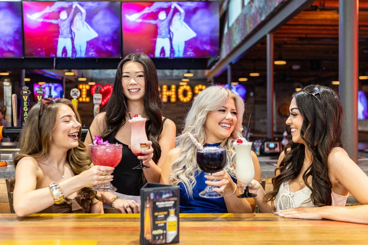 Group of friends toasting with colorful cocktails at a lively bar