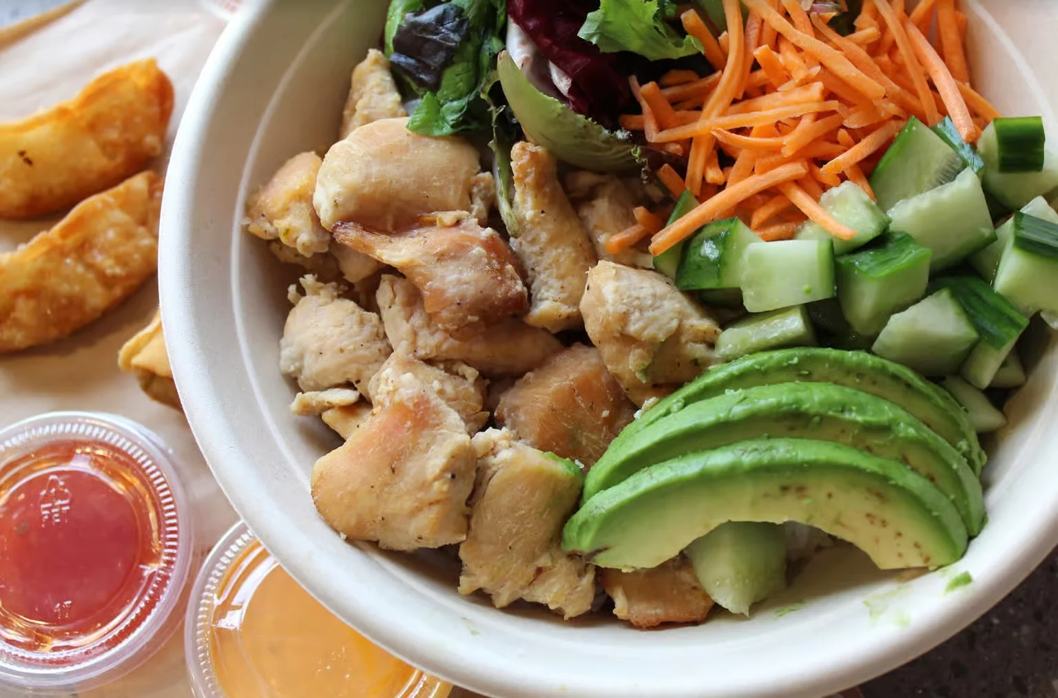 Vietnamese-style chicken bowl with spring rolls, avocado, cucumber, and carrots
