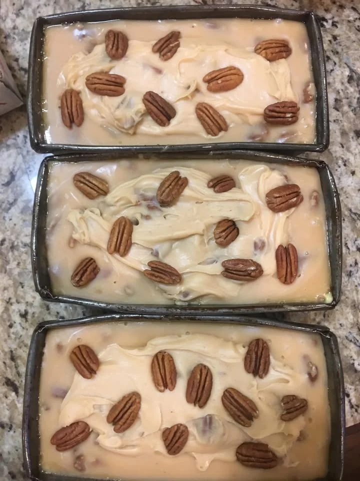 Three loaf pans filled with a creamy dessert mixture, topped with pecans and featuring a smooth surface.