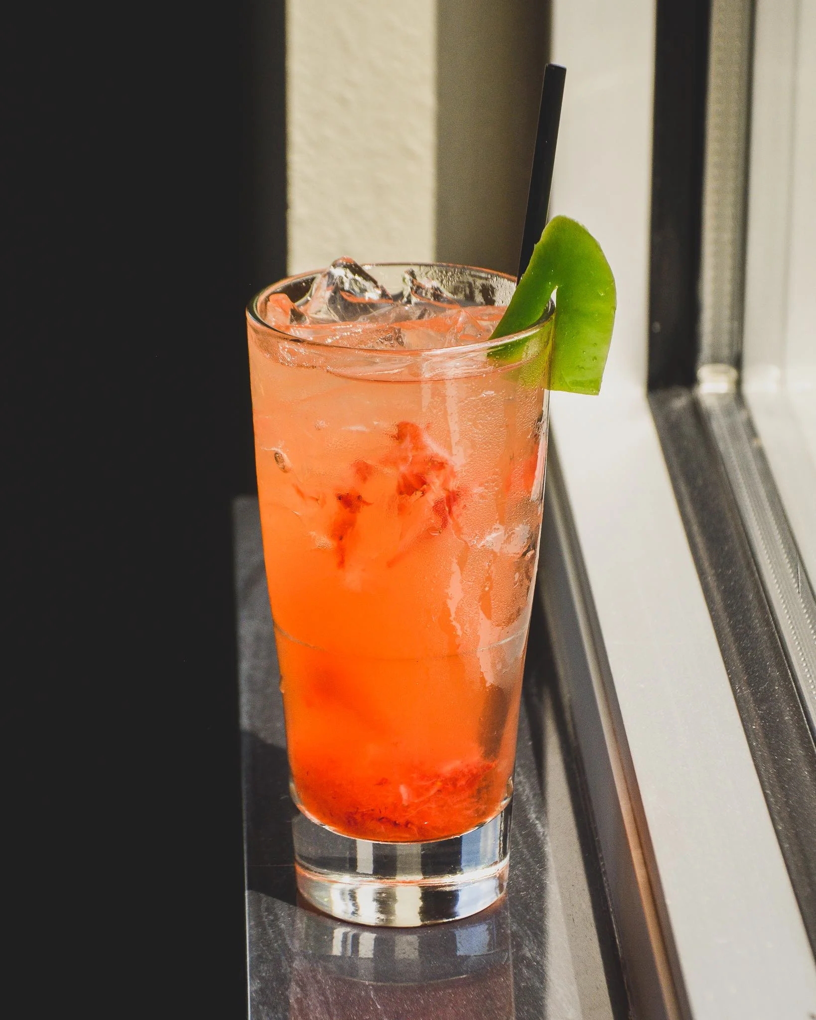 Jalapeno Business cocktail on a windowsill with pieces of strawberry and a slice of grilled jalapeno on the rim