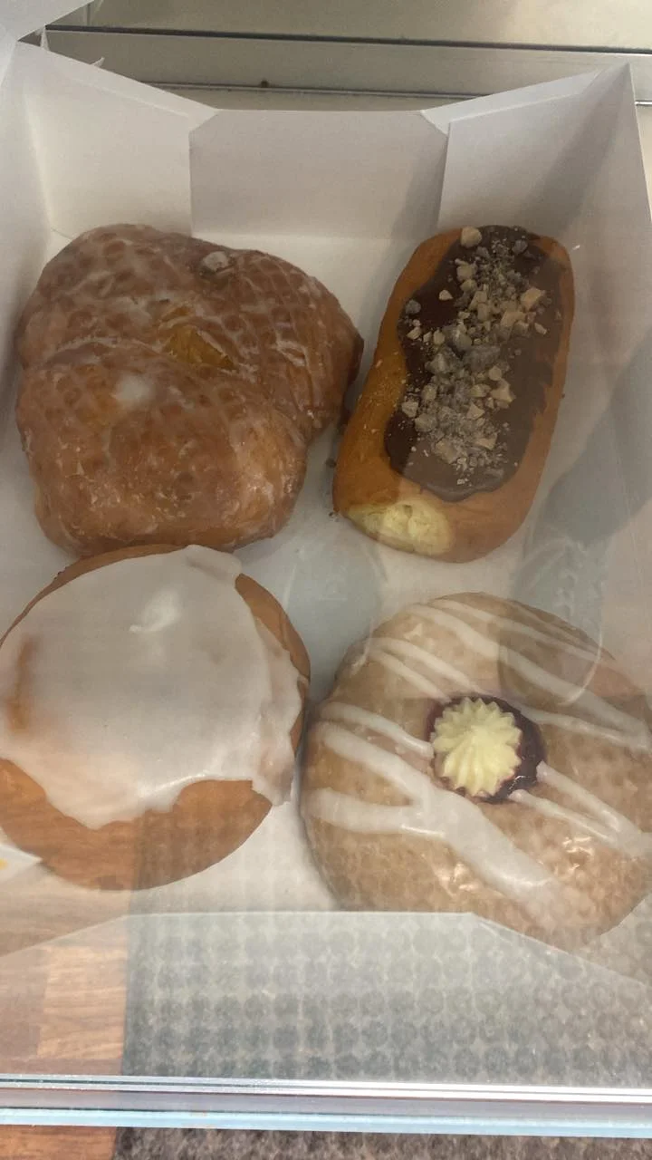A variety of four pastries including glazed donuts and filled pastries in a white box.