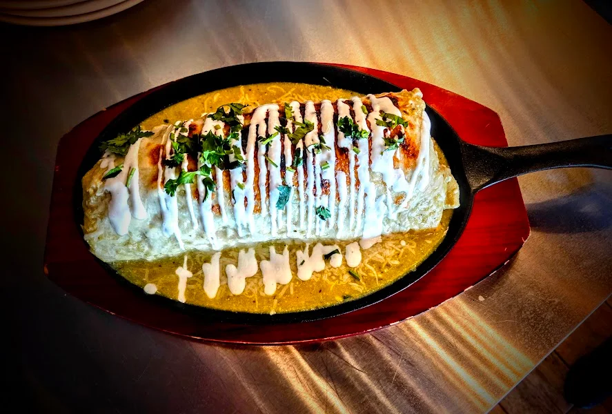 A large burrito served on a sizzling platter, topped with a drizzle of sour cream and garnished with fresh herbs.