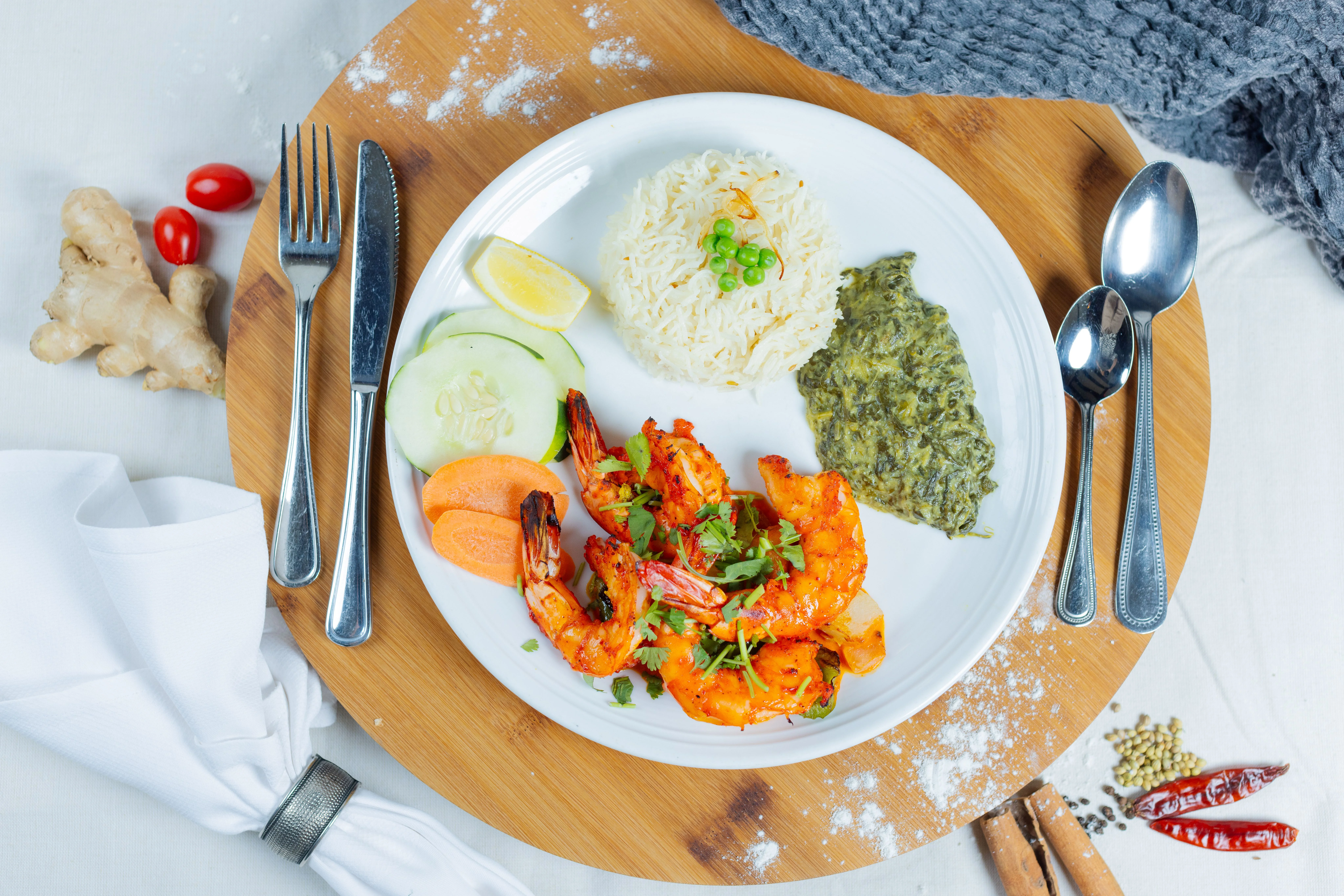 Indian seafood dish Jingha Kebab with grilled shrimp, basmati rice, palak spinach curry, cucumber, carrot, and lemon garnish served on a white plate.