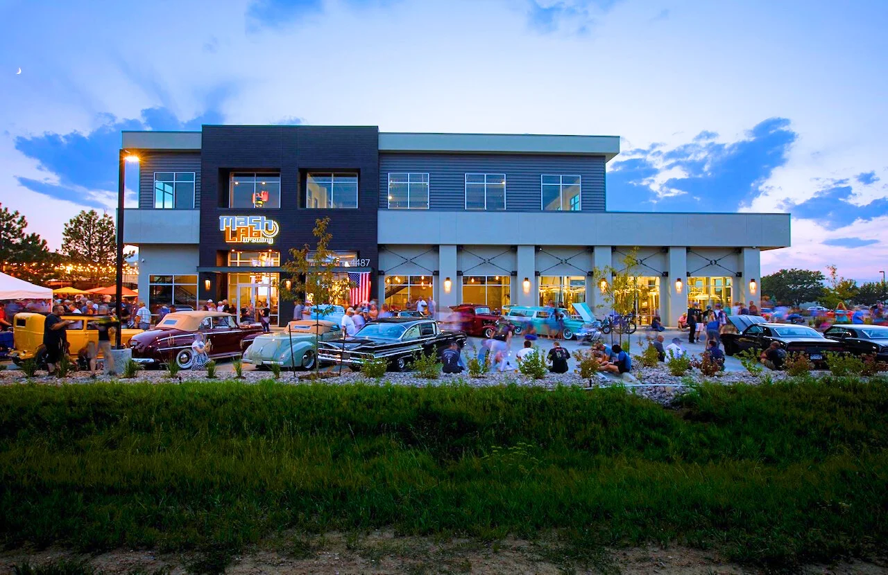Modern restaurant exterior with classic cars and lively crowd