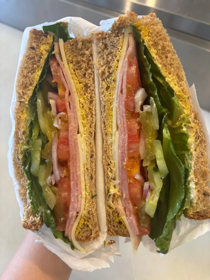 A cross-section of a sandwich made with whole grain bread, filled with layers of lettuce, tomatoes, pickles, meat, and cheese.