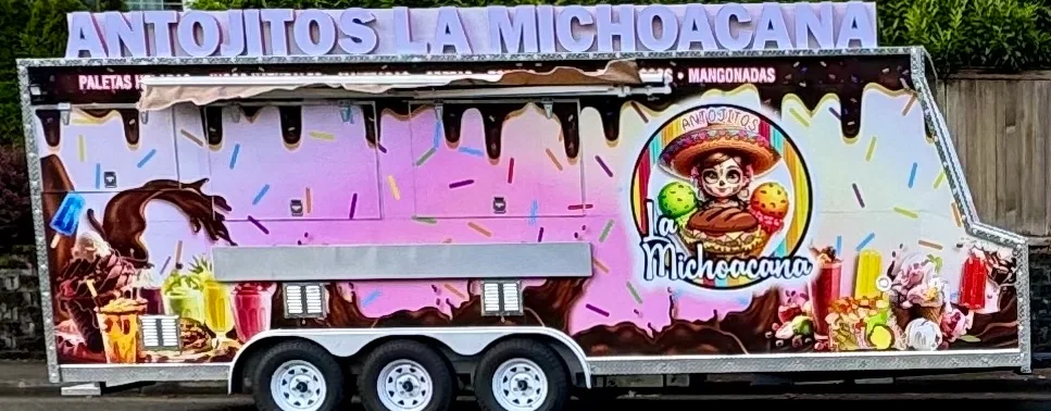 A colorful food truck displaying various dessert options, including ice cream and paletas, decorated with vibrant graphics and a playful design.