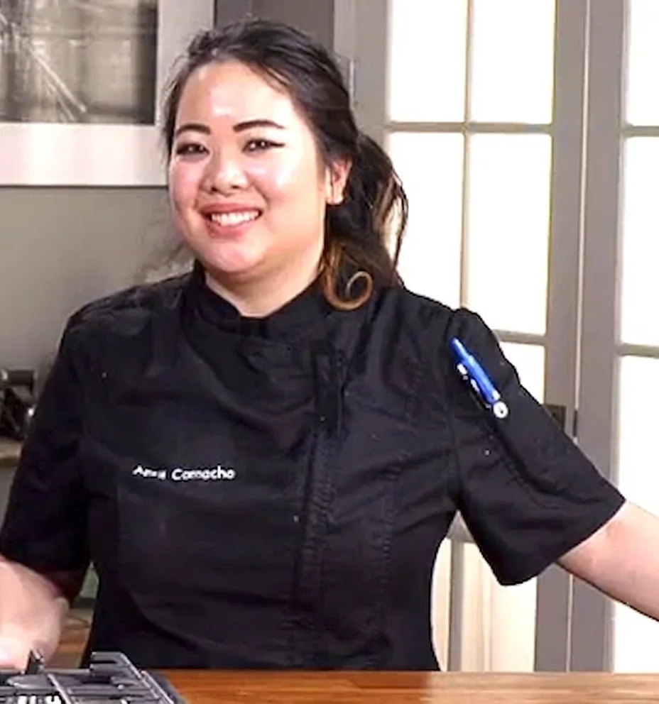 A chef in a black chef's coat smiling at camera for a tv shoot