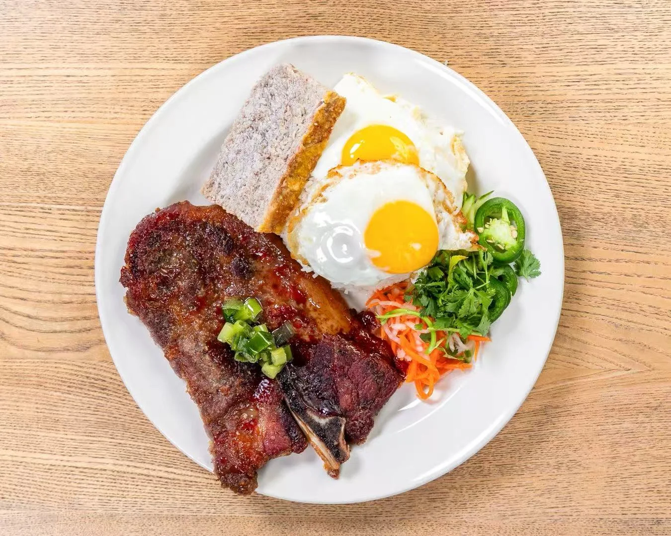 Plate of grilled meat, fried eggs, vegetables, and bread on a wooden table.