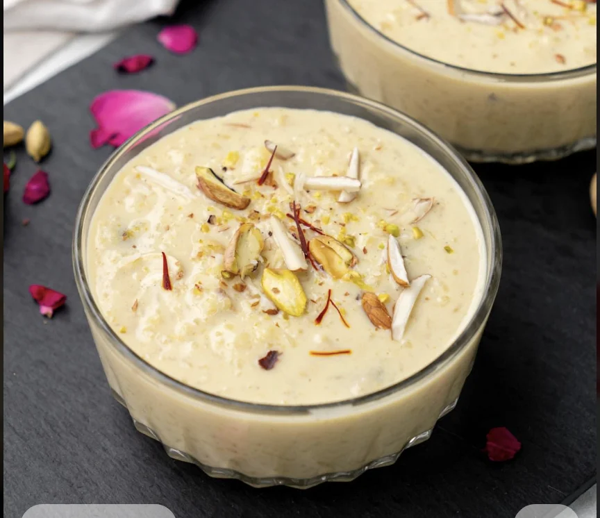 A creamy dessert topped with nuts and saffron strands served in a glass bowl.