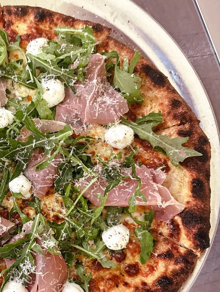 Italian prosciutto pizza topped with arugula and mozzarella