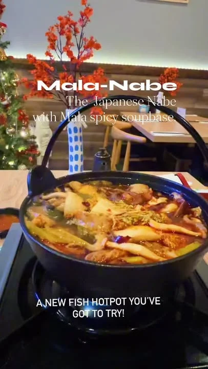 A hot pot dish featuring various ingredients submerged in a spicy mala broth, served in a traditional pot. The setting includes decorative branches and a cozy dining atmosphere.