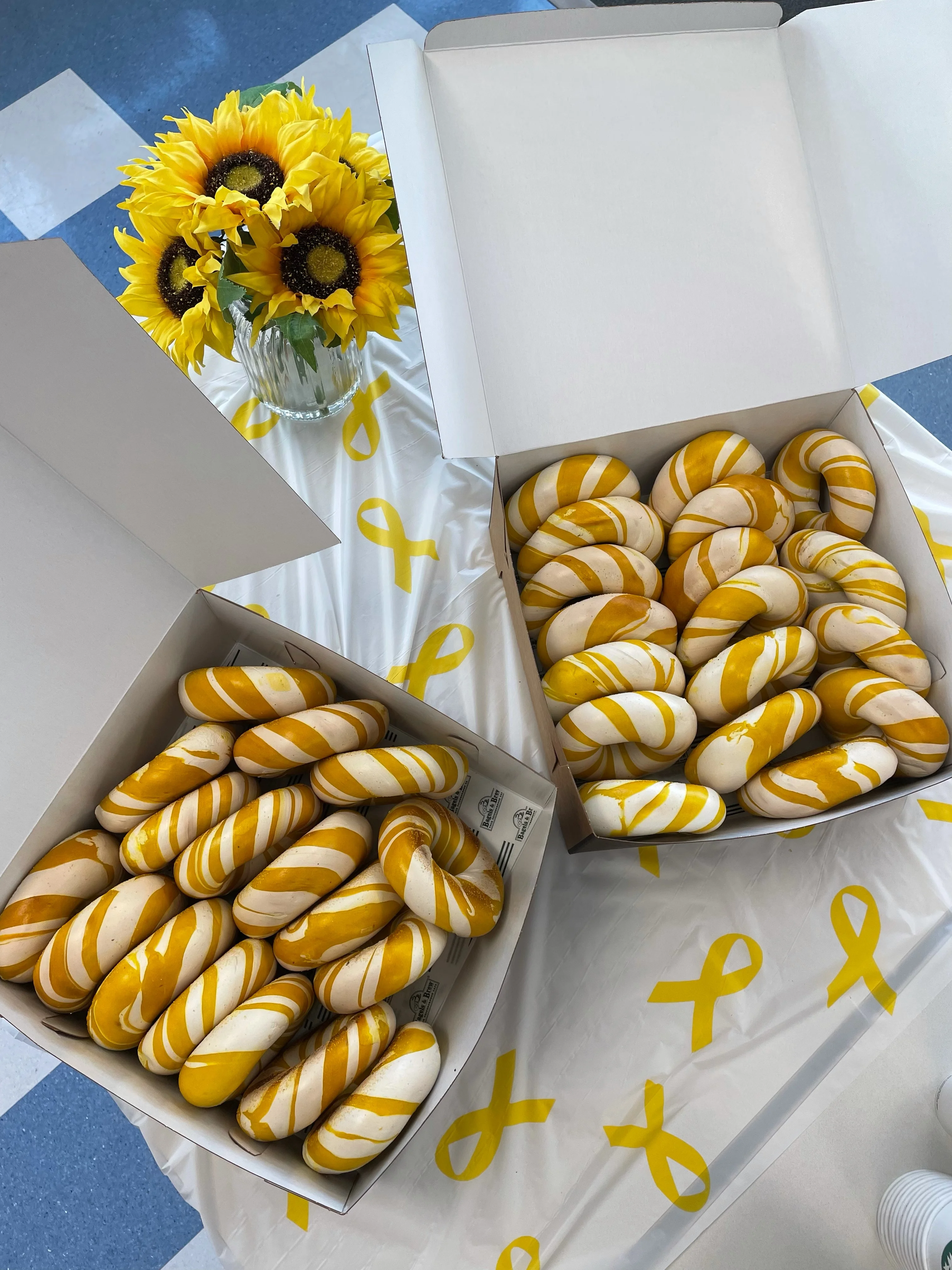 Overhead view of mustard-striped soft pretzel bites in bakery boxes with sunflowers
