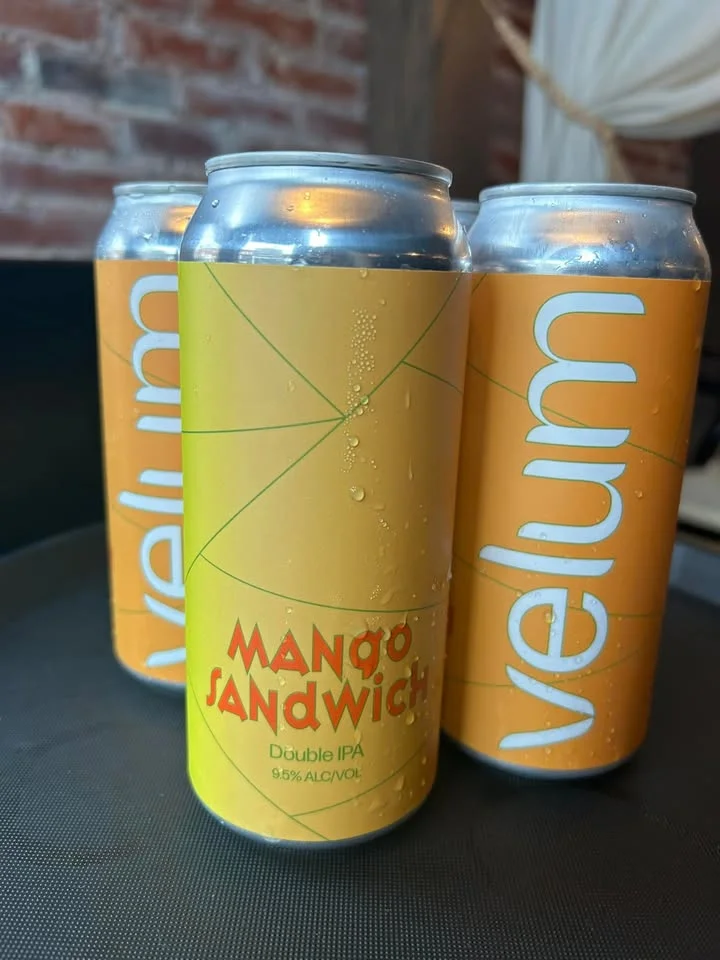 Cans of mango-flavored double IPA beer arranged on a table with condensation on the surface.