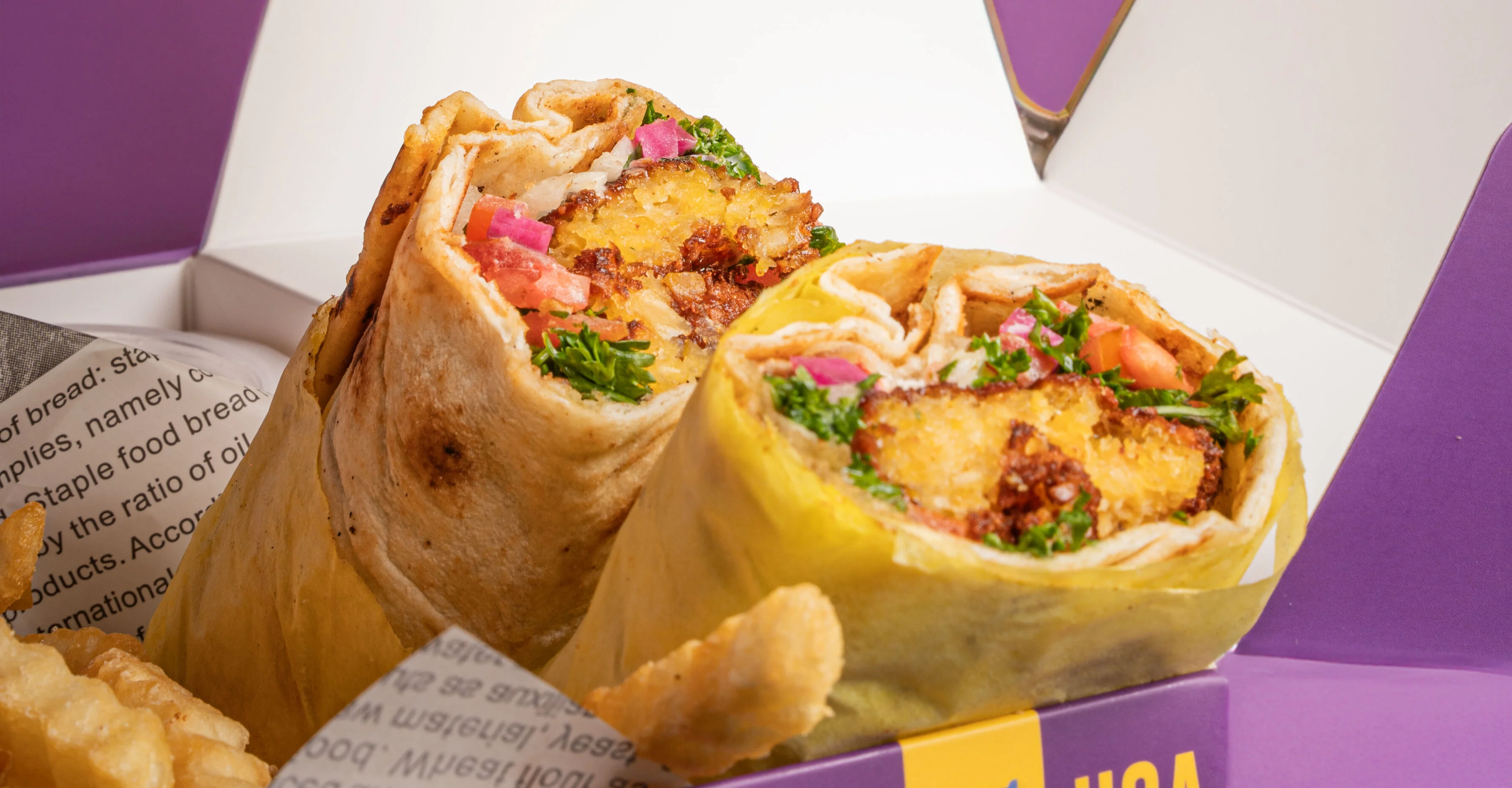Hand holding hummus over two wrapped burritos in a takeout box.