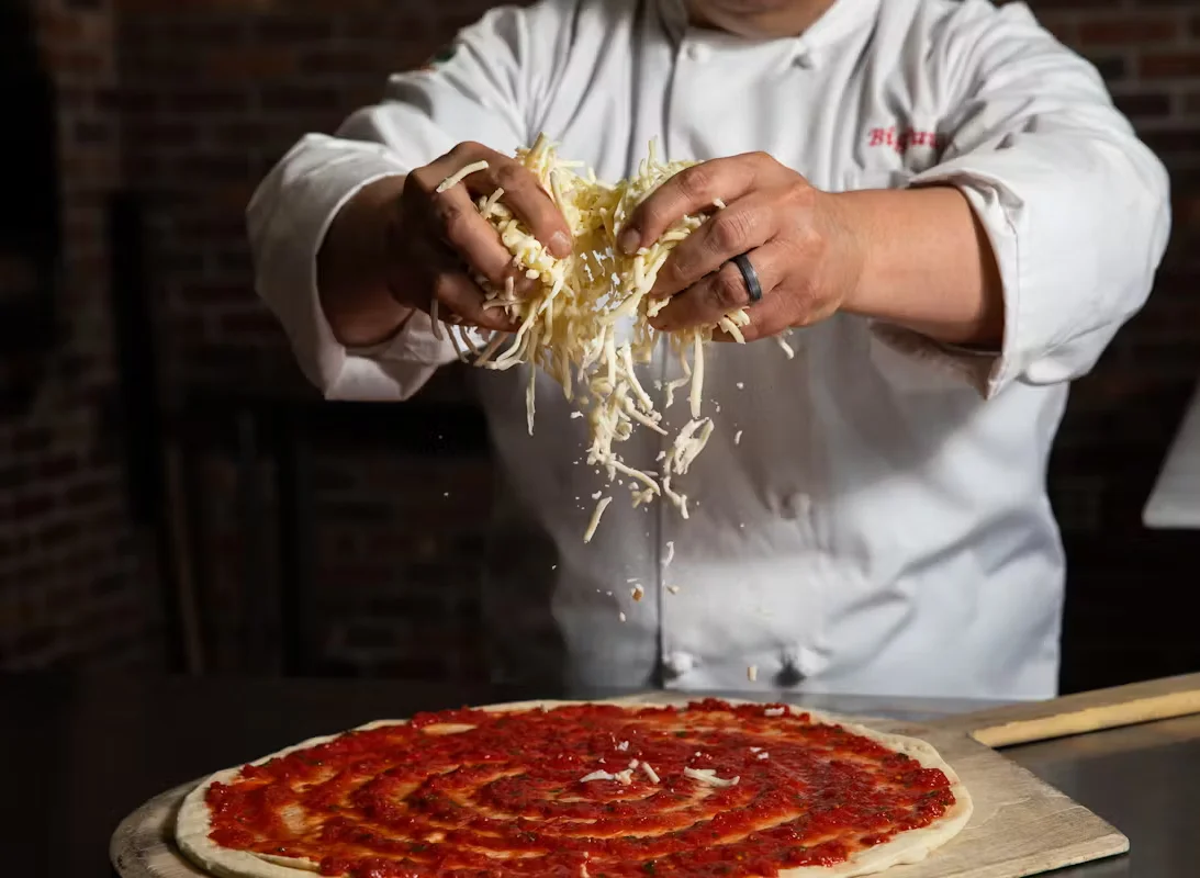 A chef adding a helping of mozzarella on a pizza