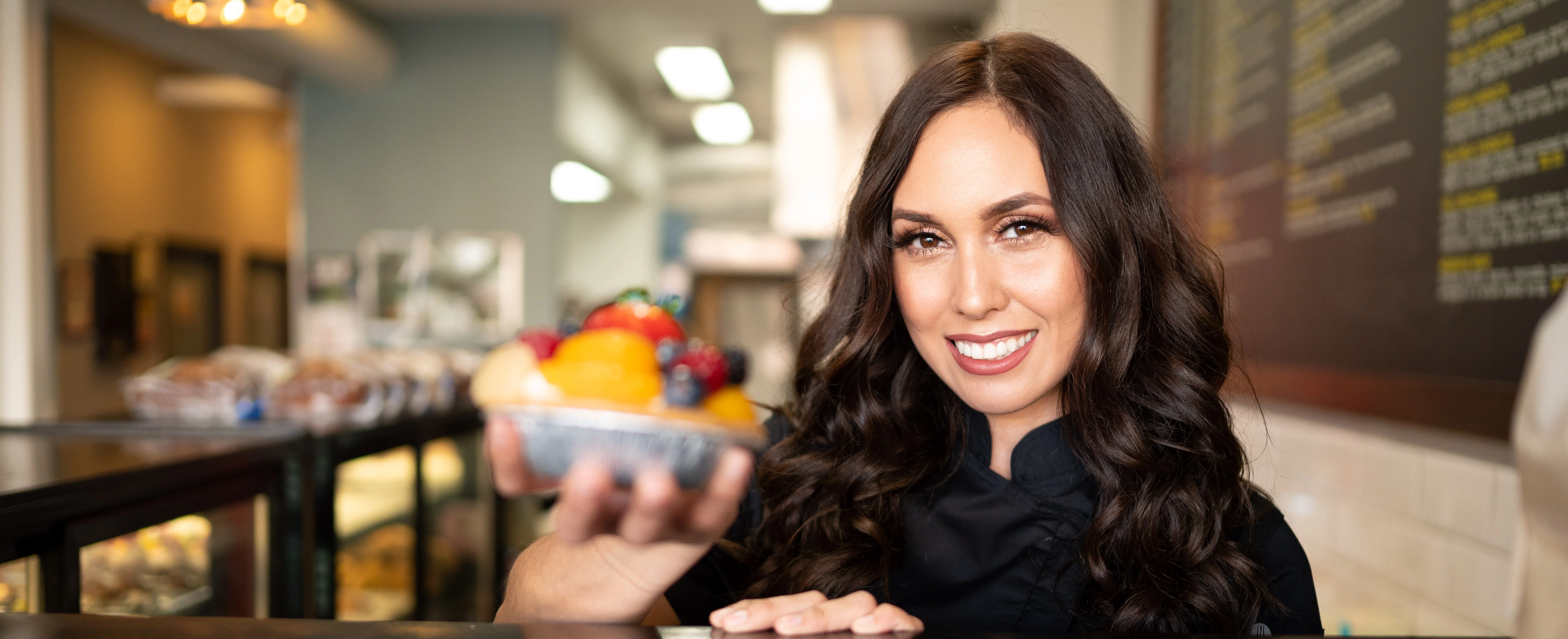Chef presenting a colorful fruit tart in a cozy café setting