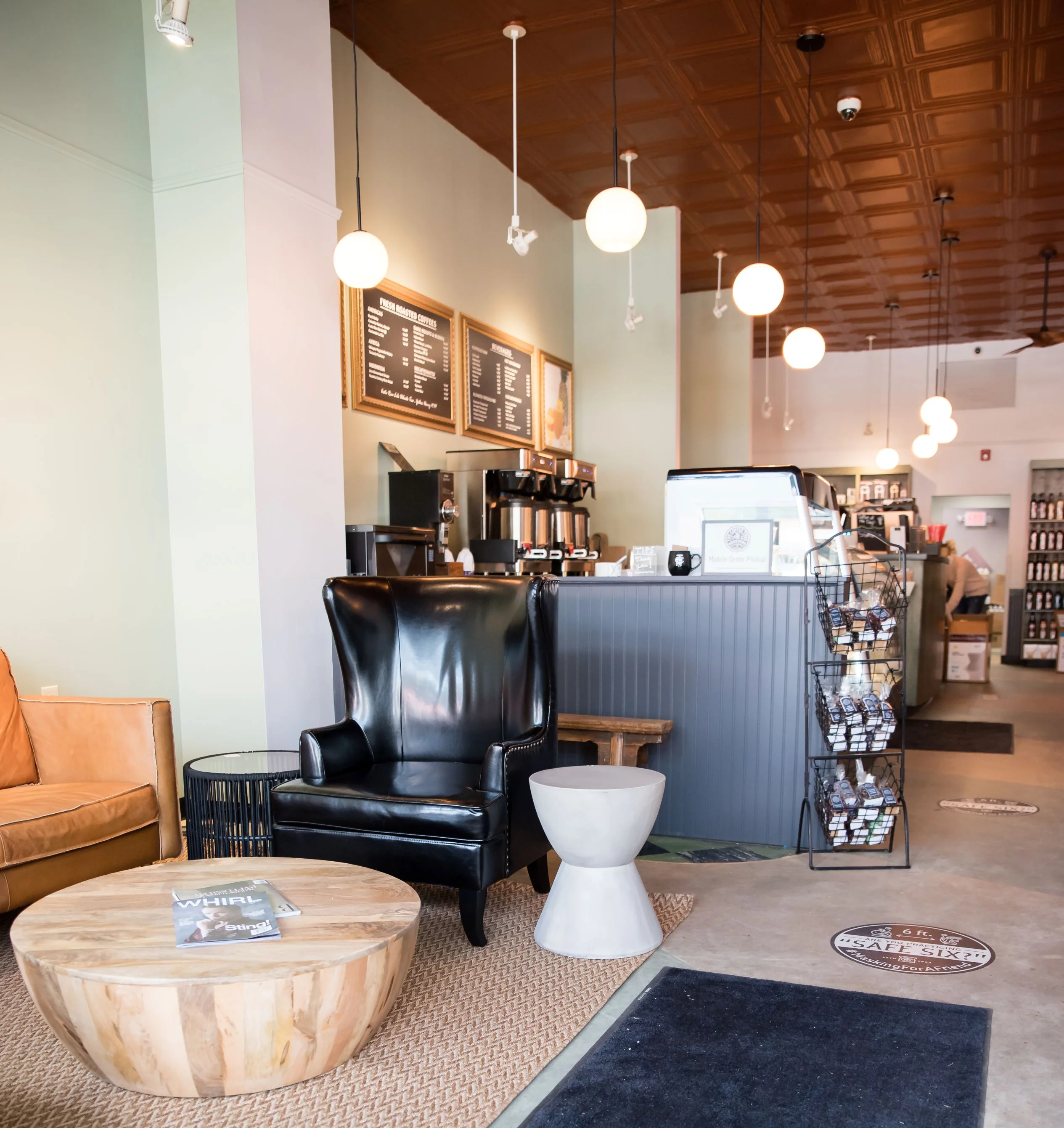 Cozy café interior with leather armchair, wooden coffee table, and hanging globes. Menu on wall, coffee machines behind the counter, serene ambiance.