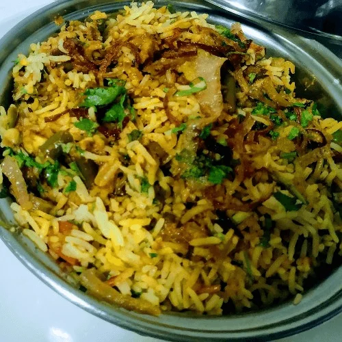 Vegetable biryani or chicken biryani in an oval metal serving dish.