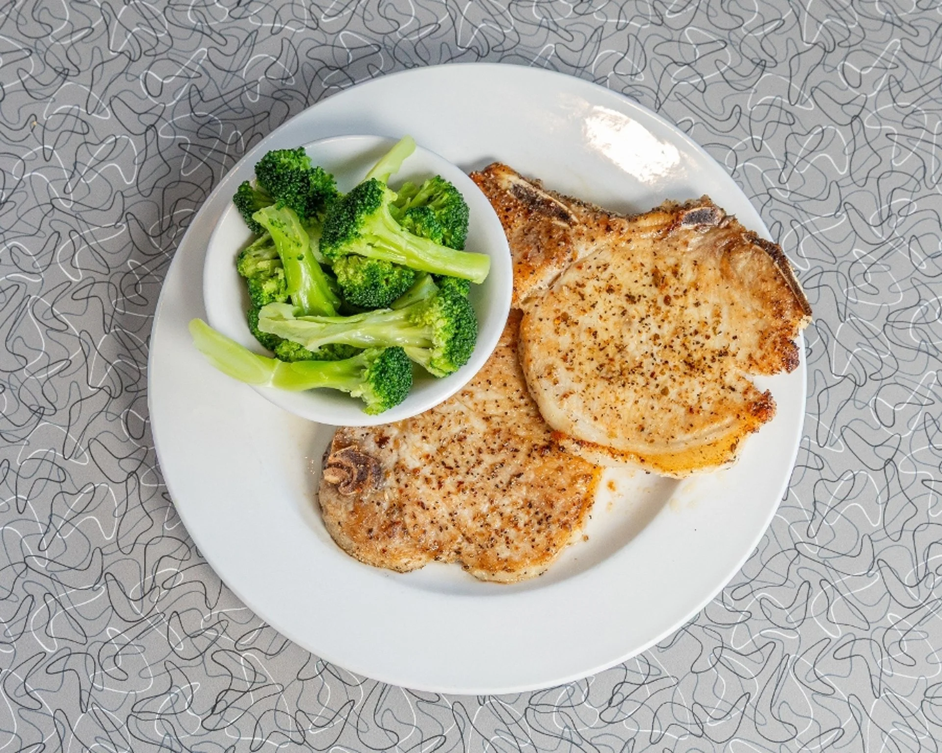 Grilled pork chops served with steamed broccoli on a white plate