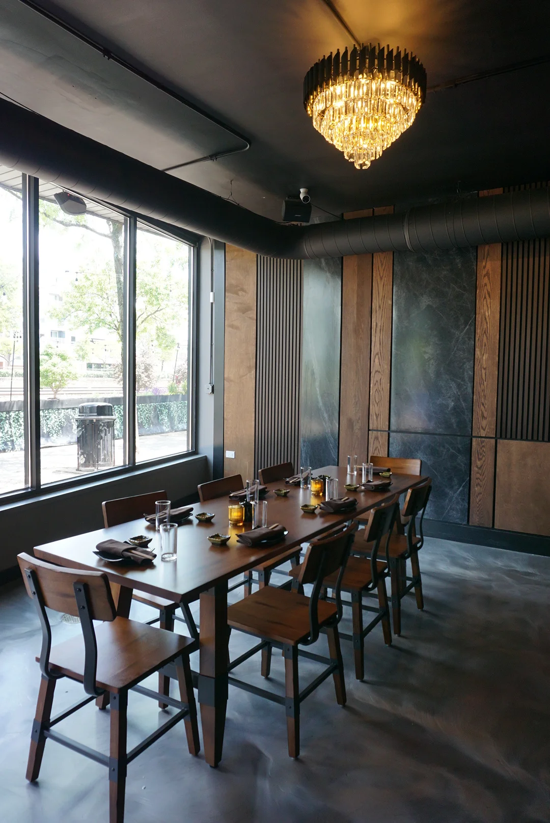 Modern restaurant interior with a long wooden dining table and elegant chandelier.
