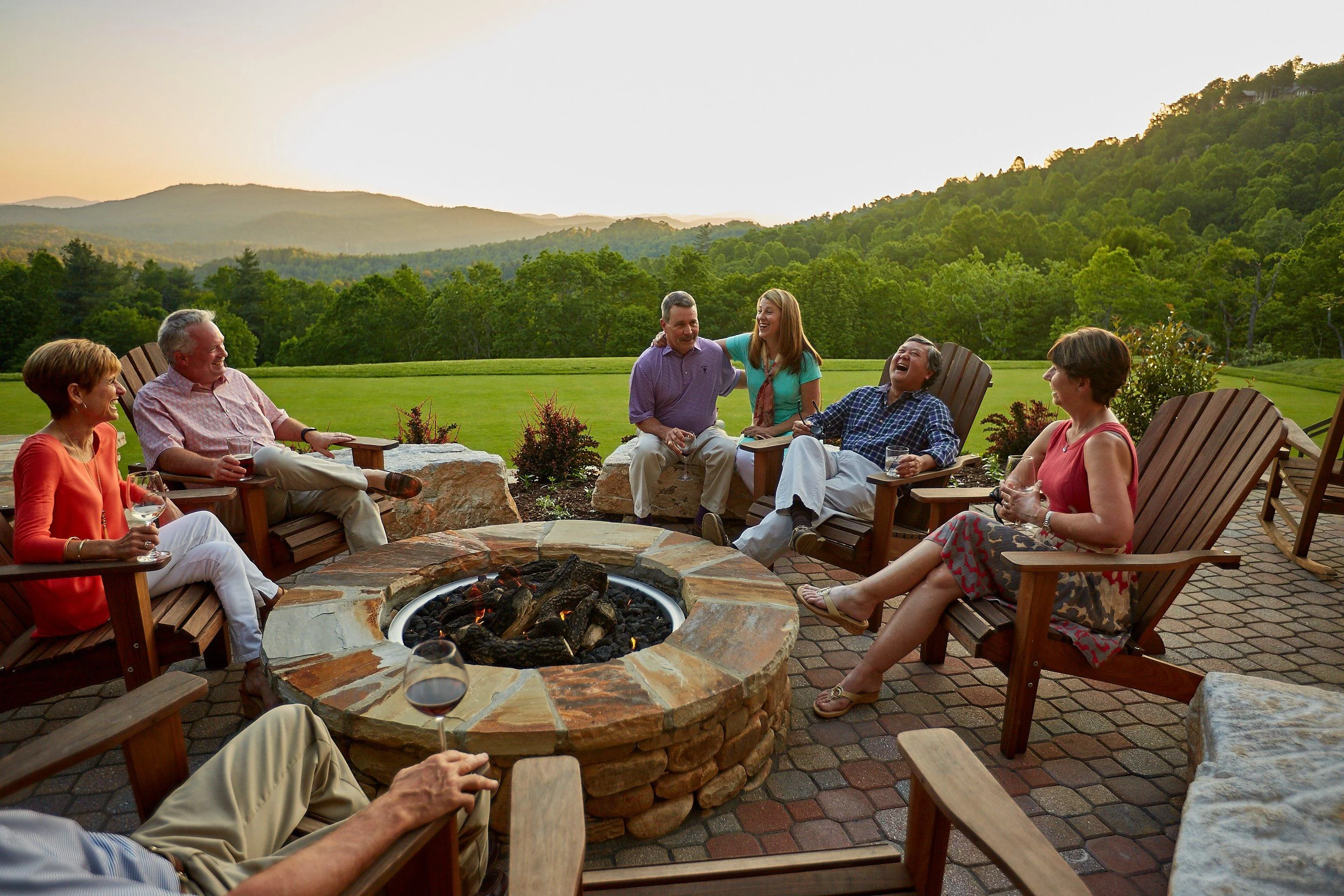 Group of friends enjoying drinks by a fire pit at sunset