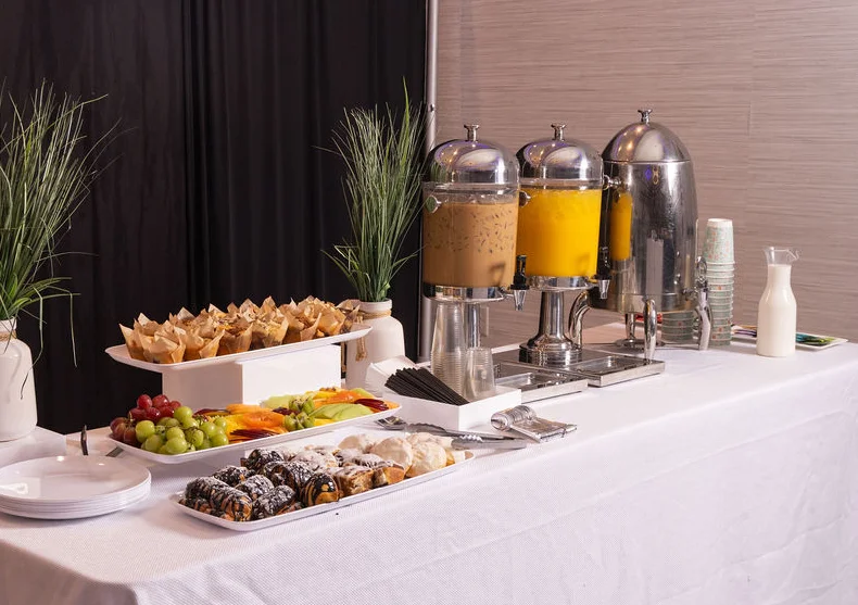 Buffet table with drinks, pastries, and fresh fruit on a white tablecloth.