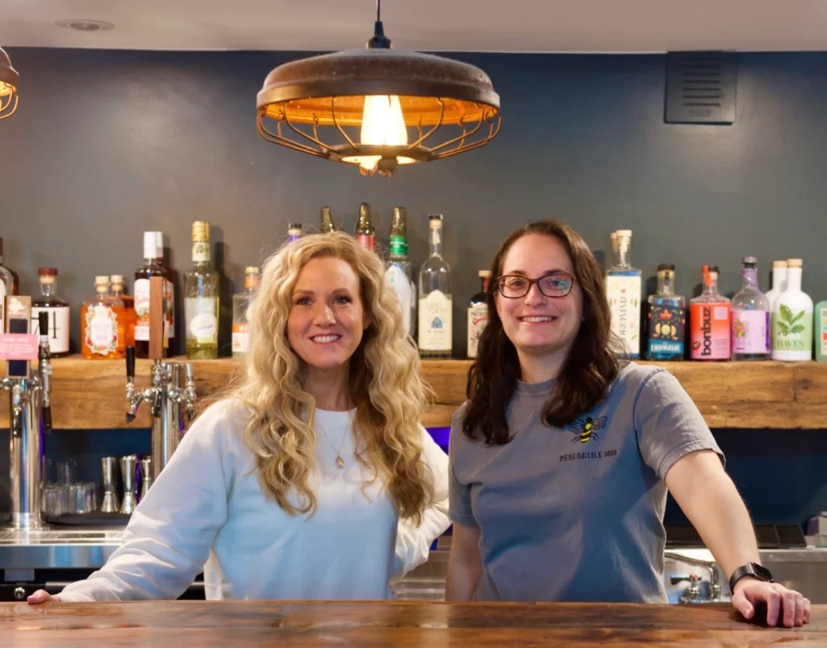 Bartenders smiling behind a stylish bar with various spirits