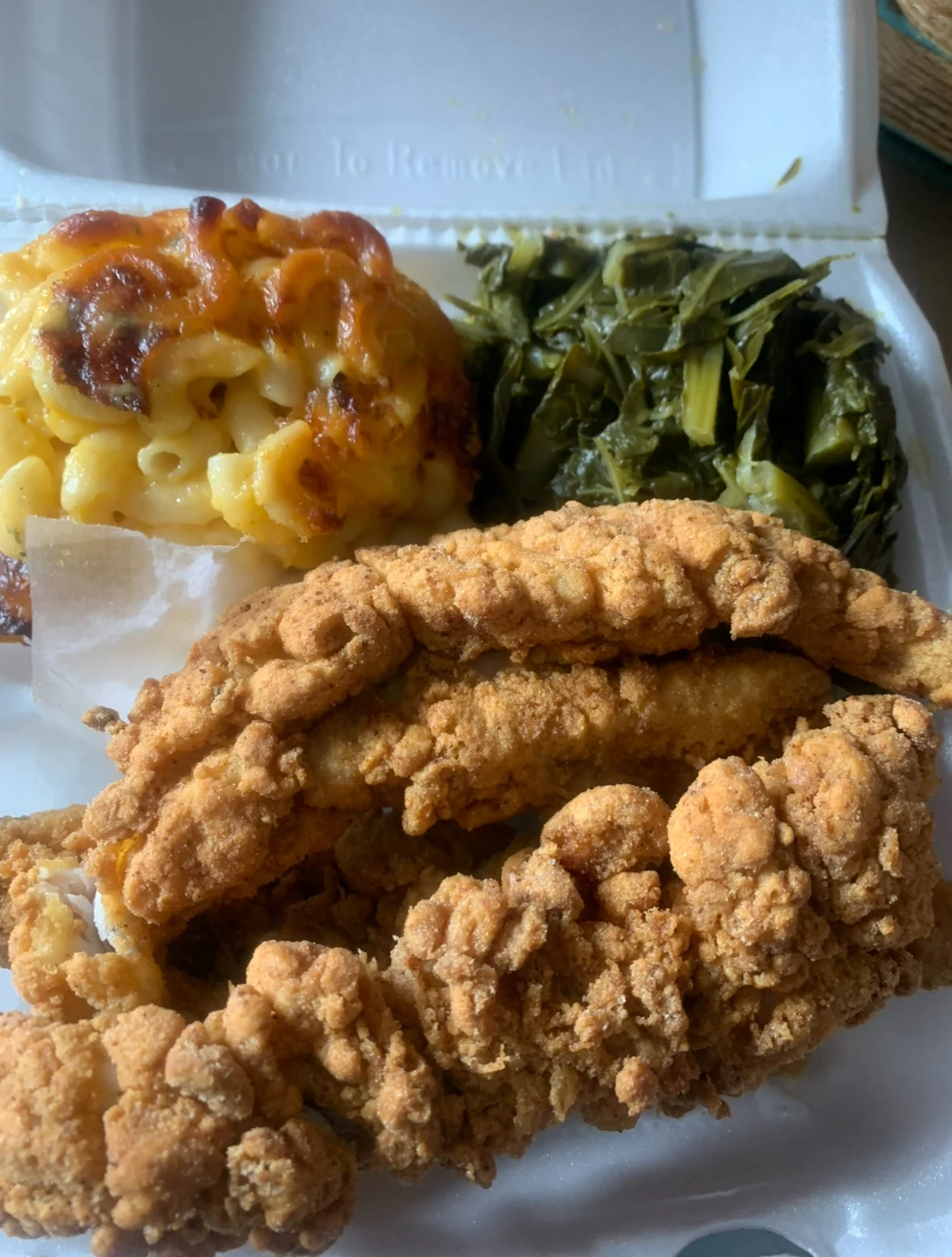 A takeout container filled with crispy fried fish, macaroni and cheese, and collard greens.