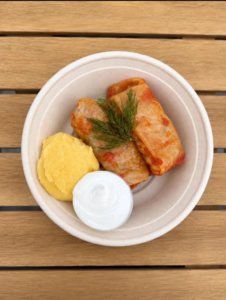 A dish consisting of stuffed cabbage rolls served with polenta and a dollop of sour cream, garnished with fresh dill.