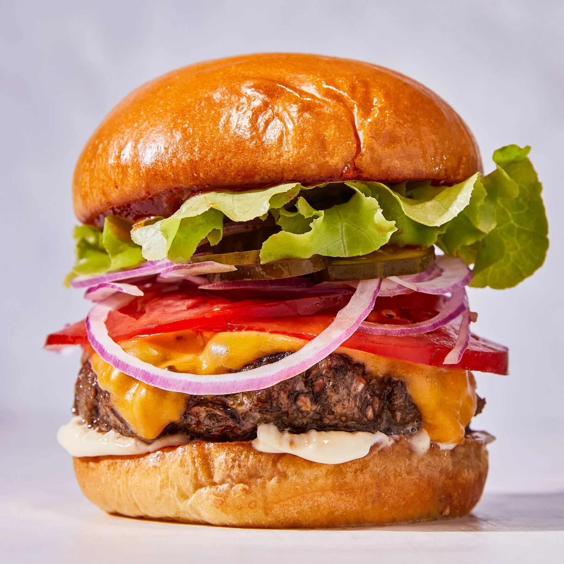 A delicious burger stacked with a juicy beef patty, melted cheese, fresh lettuce, tomato, onions, and pickles, all contained within a shiny bun.