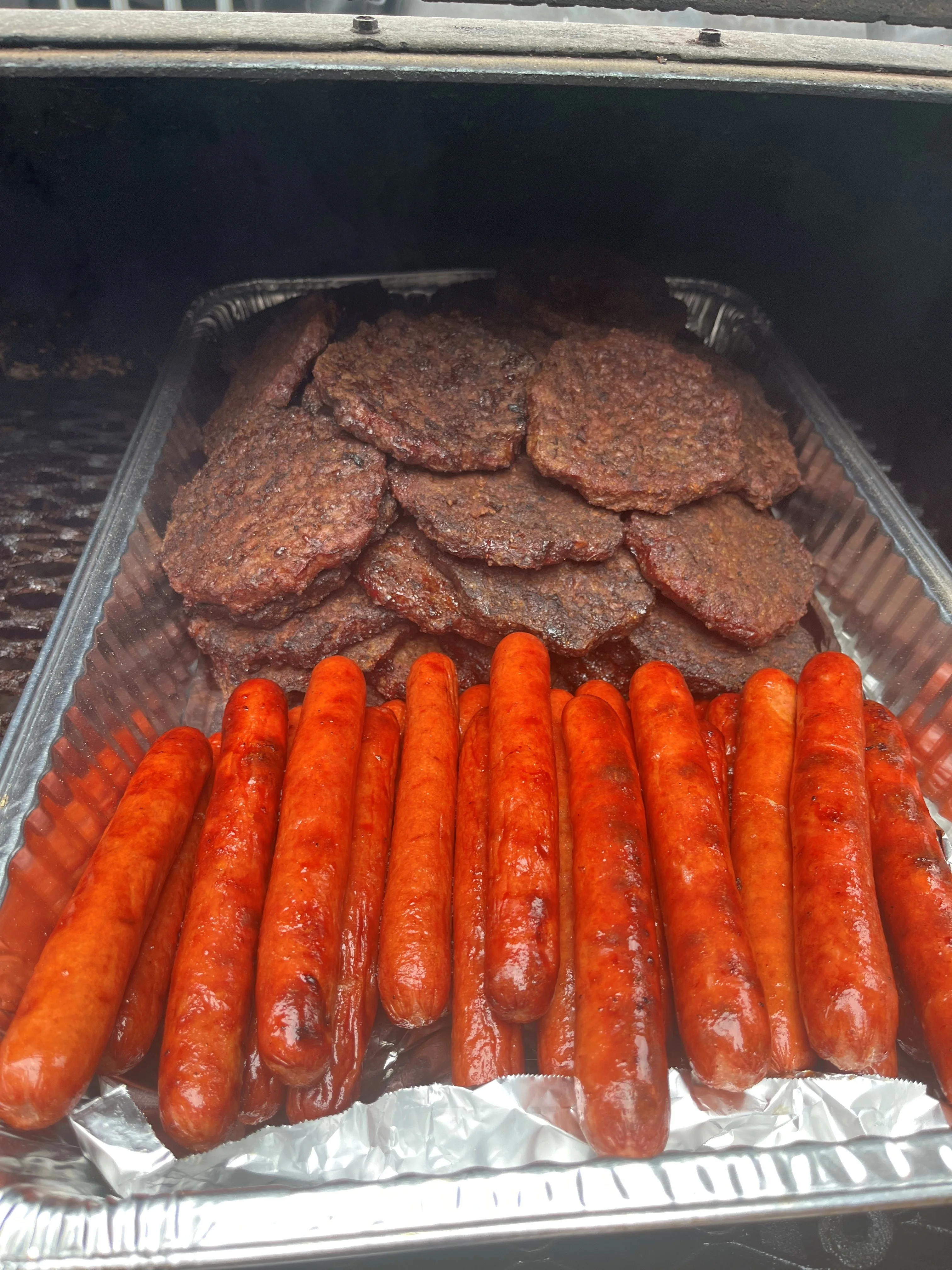 Grilled sausages and beef patties arranged in a tray, showcasing a smoky barbecue preparation.
