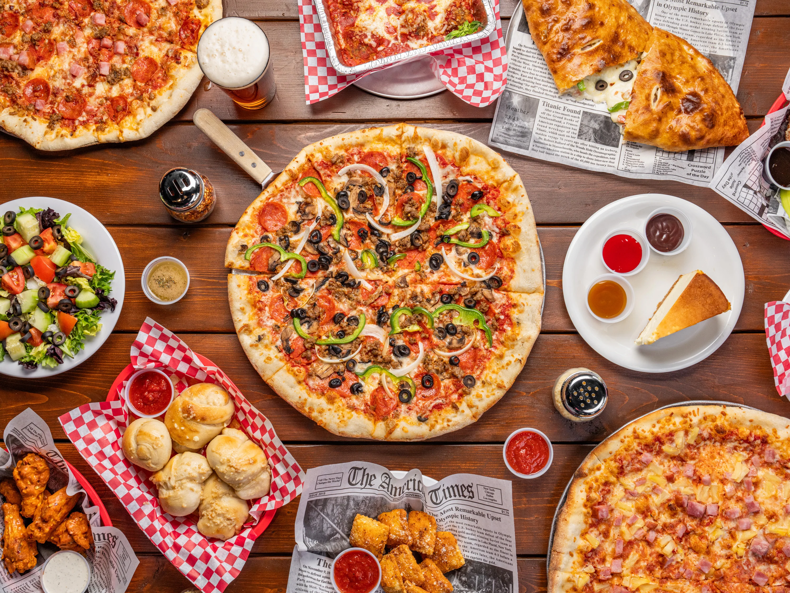 A vibrant and inviting display featuring an assortment of New Braunfels' best pizza: a supreme pizza adorned with a variety of toppings, alongside craft beer, golden garlic knots, a fresh garden salad, and crispy fried ravioli, all arranged tastefully on a table setting that promises a delightful dining experience.