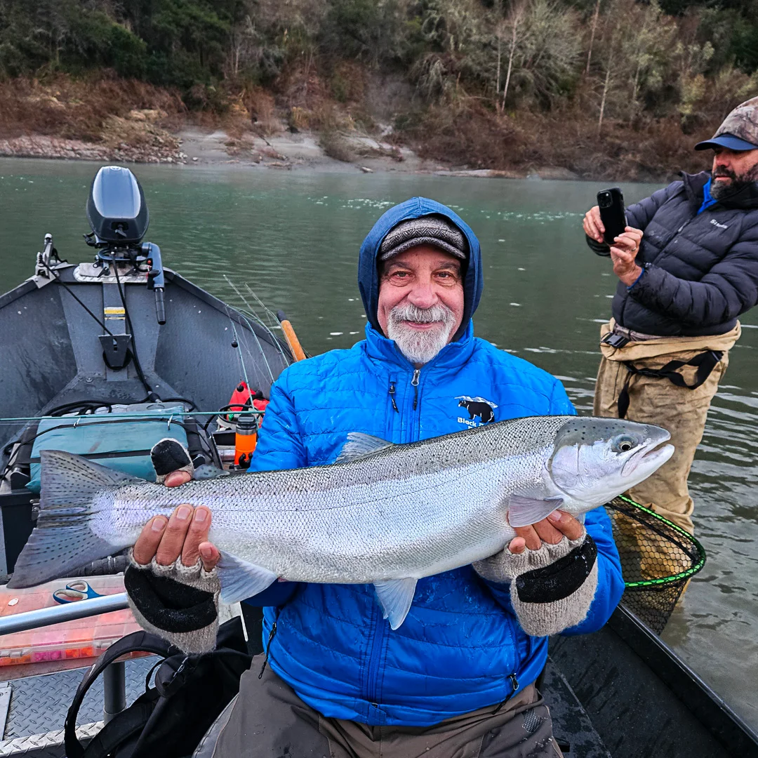 Angler proudly holding a large steelhead trout in a boat