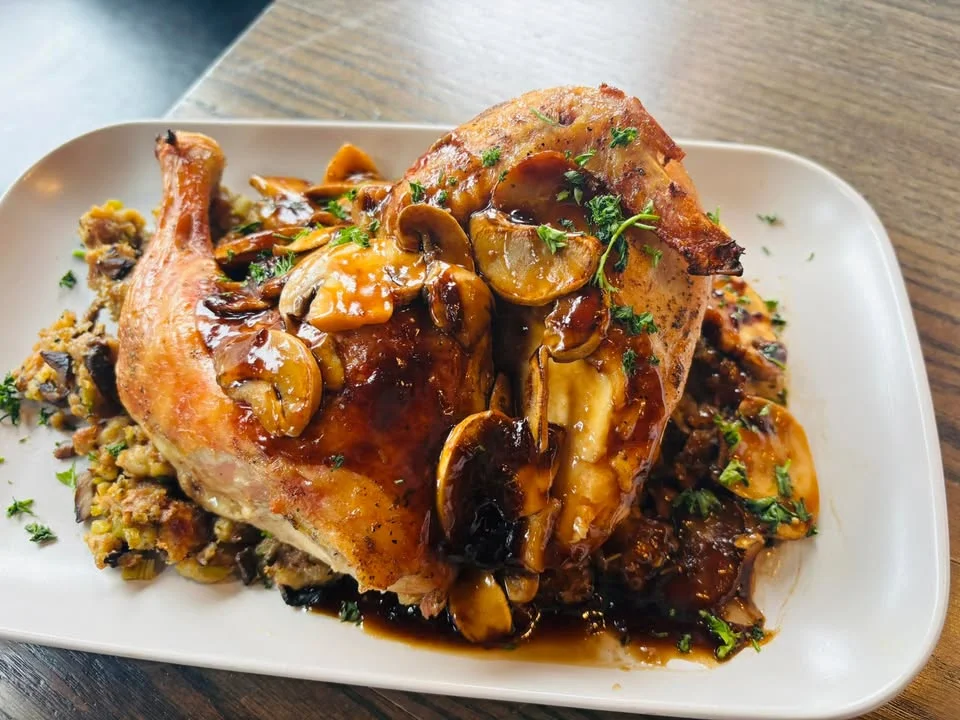 A plate of roasted chicken served with flavorful mushroom gravy and stuffing, garnished with herbs.