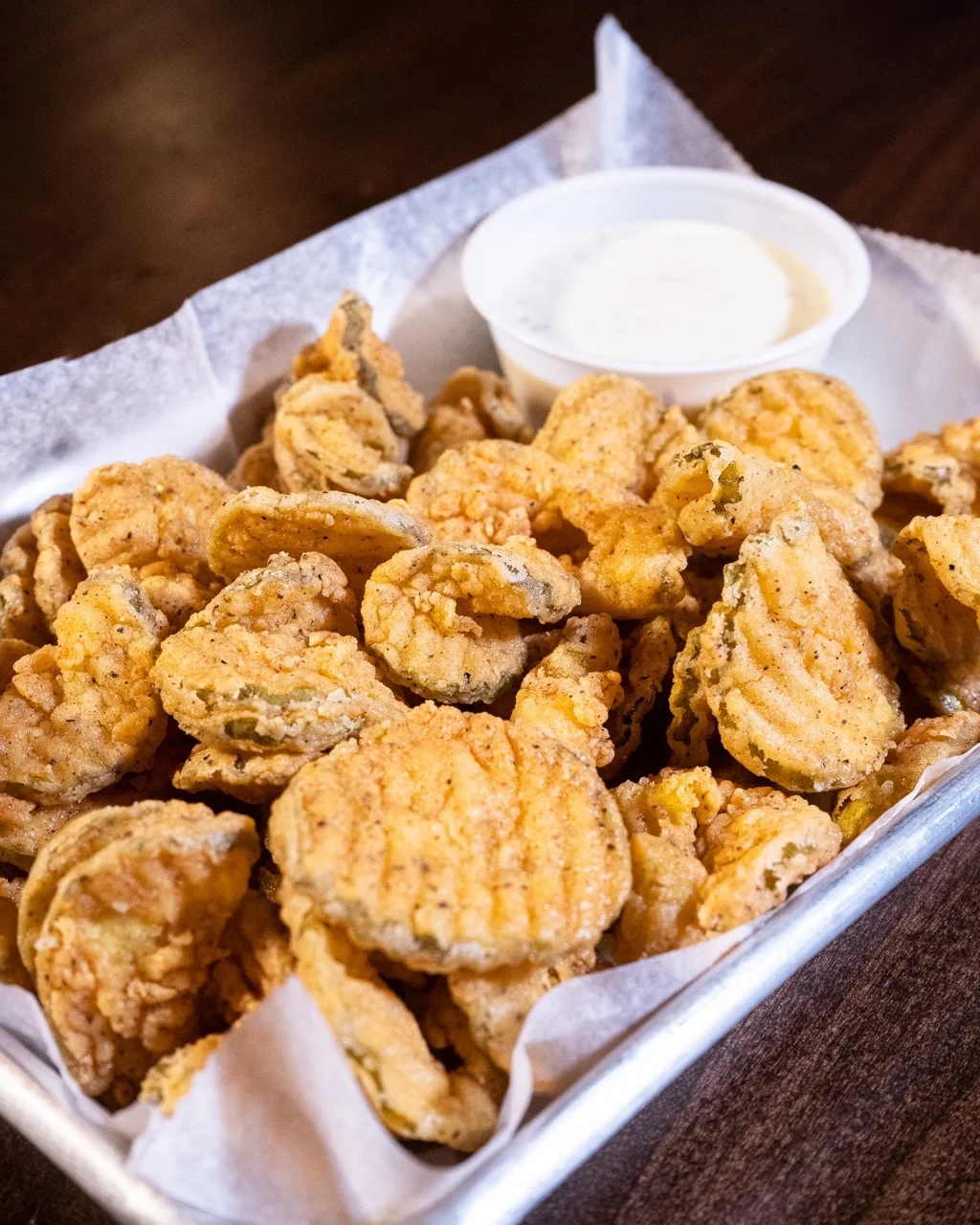 A tray of crispy fried pickles served with a side of ranch dressing.