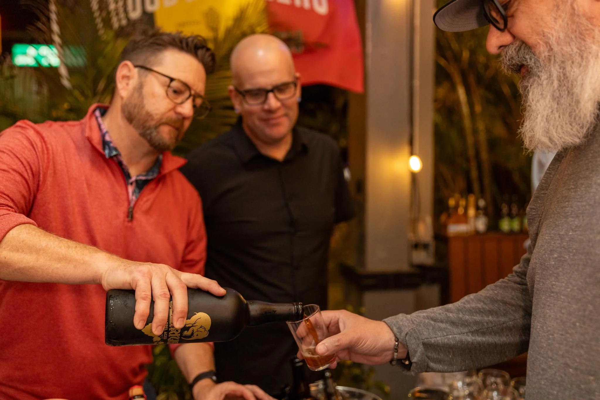 Bartenders pouring drinks at a lively bar event with tropical decor.