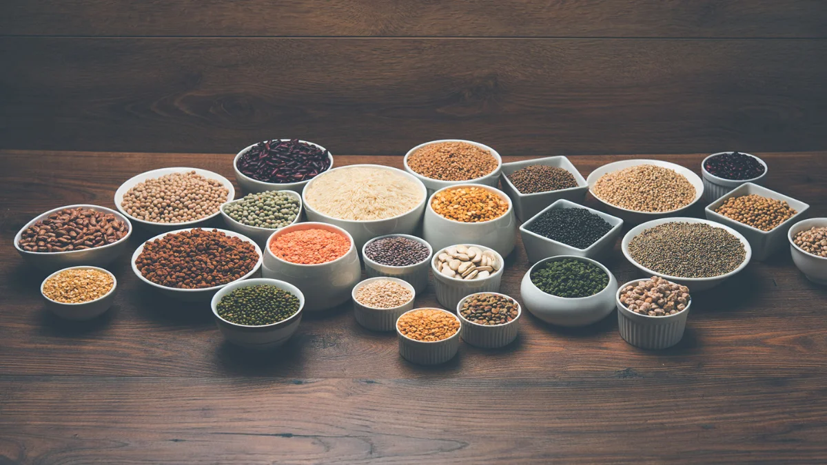Variety of lentils and grains in white bowls on a wooden table