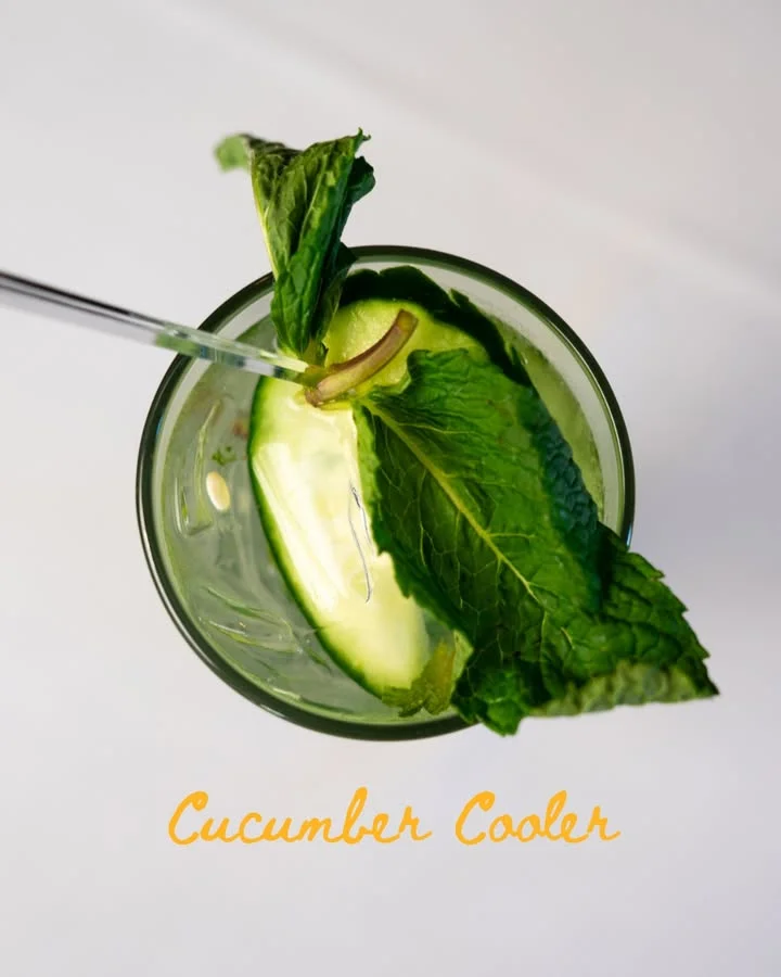 A refreshing drink with cucumber slices and mint leaves, presented in a clear glass with ice.
