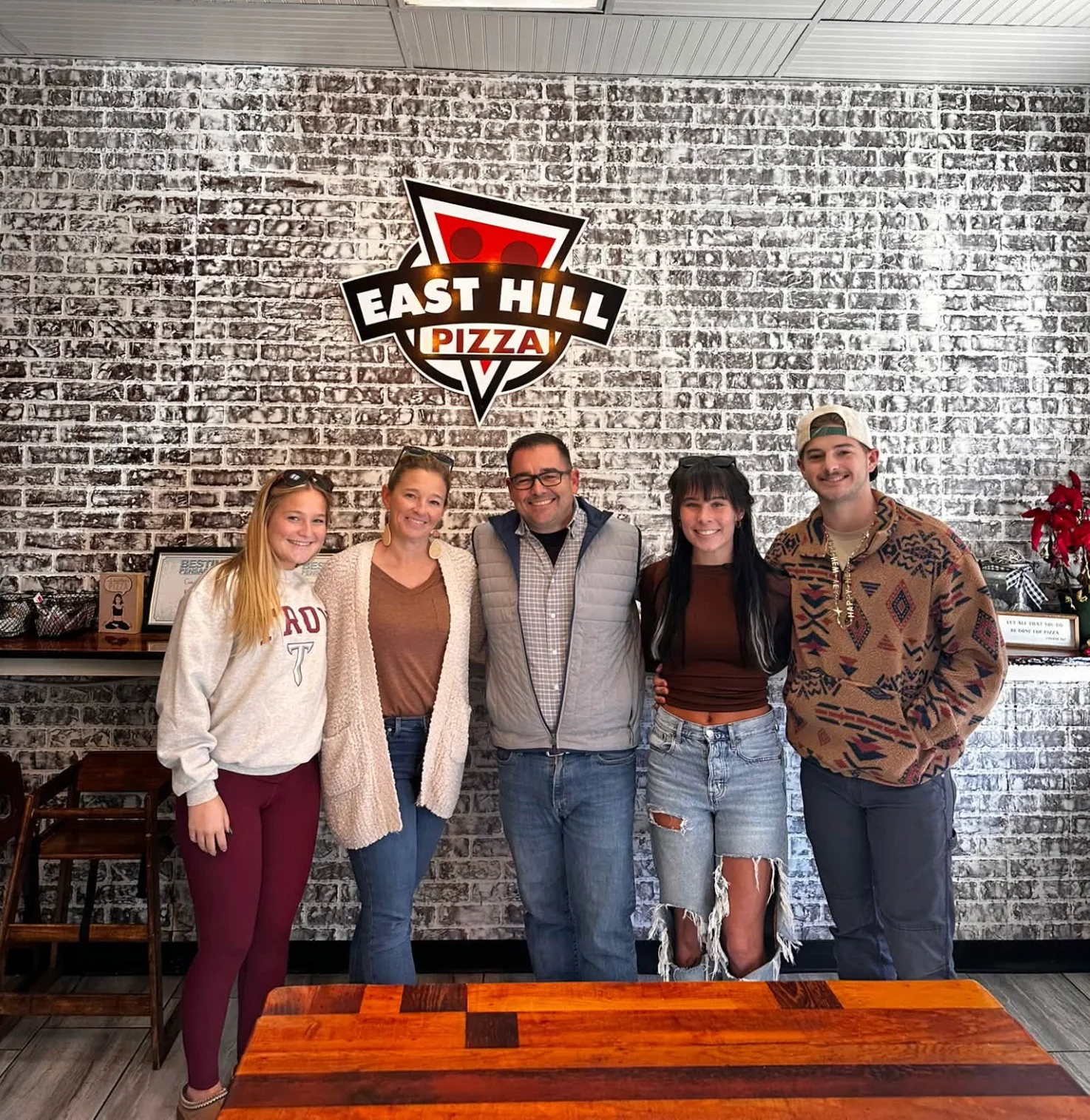 Restaurant team posing beneath a pizza parlor logo on a brick wall