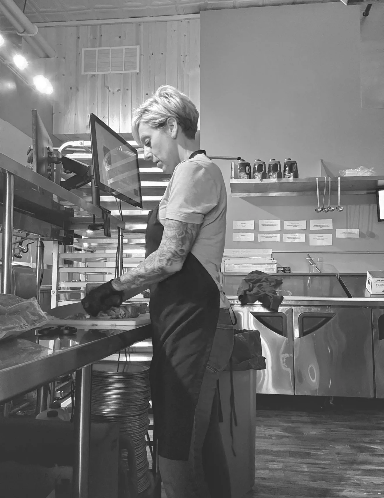 A woman in an apron preparing ingredients on a stainless steel counter in a restaurant kitchen.