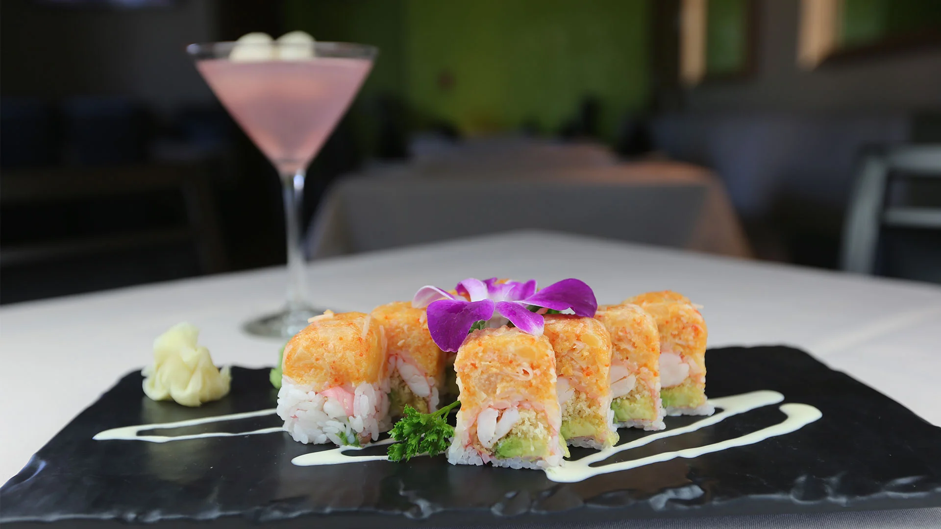 Colorful sushi rolls on a black plate with a cocktail in the background