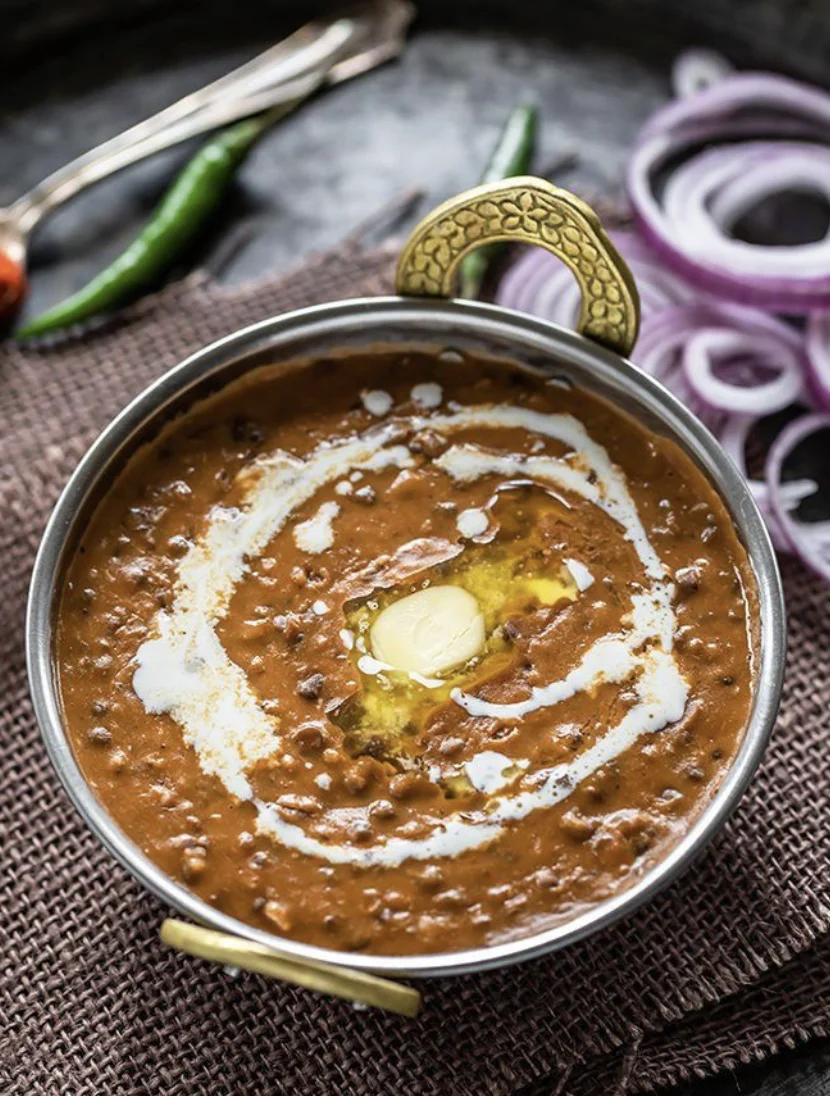 A bowl of lentil curry with a drizzle of cream and butter on top, surrounded by green chilies and red onion slices.