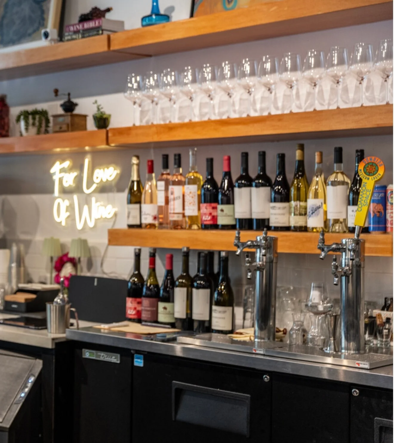 Wine bar with shelves of wine bottles and glasses, illuminated sign 'For Love Of Wine'