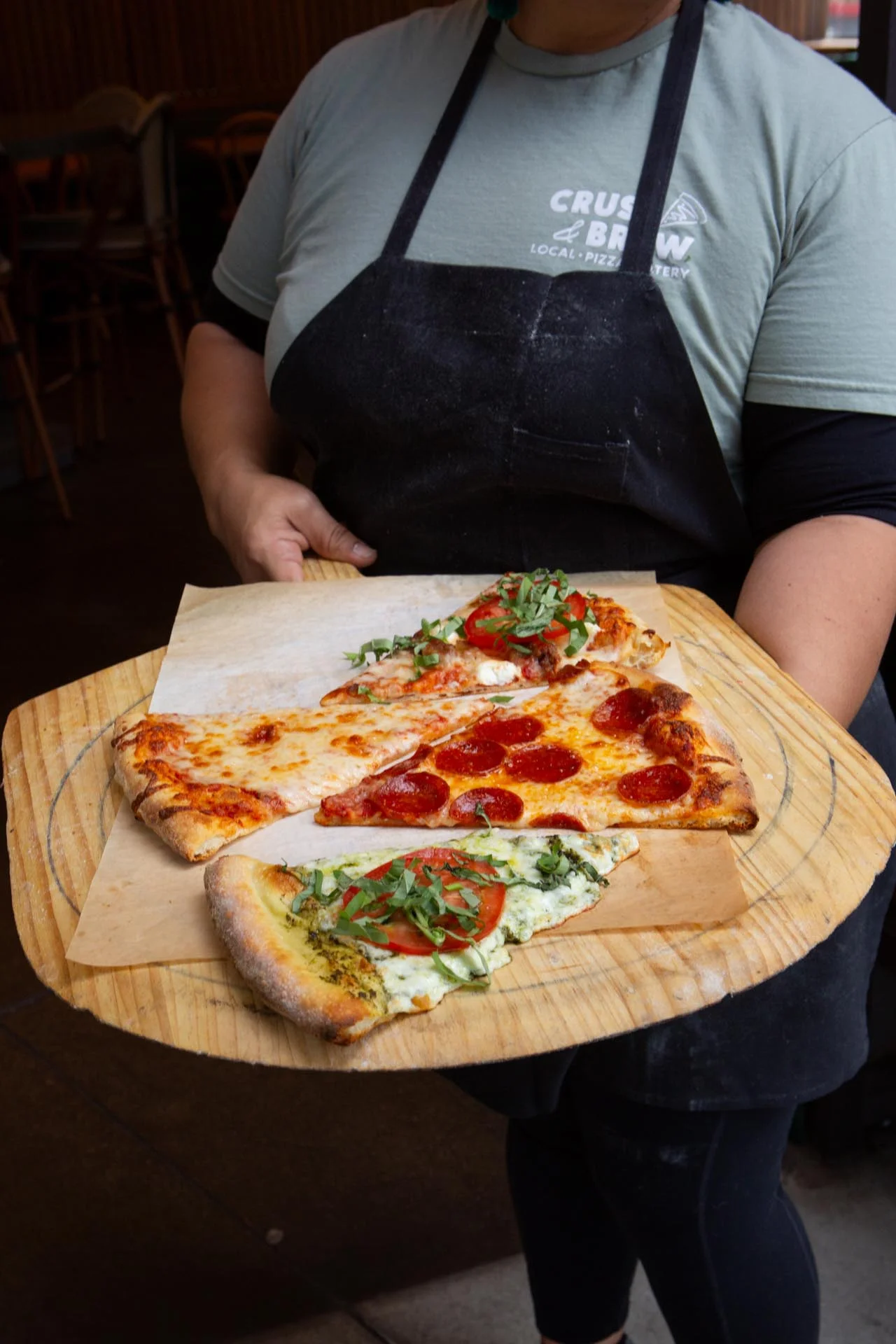 A group of hands reaching for slices of pepperoni pizza from a large serving tray, set on a table with empty plates.