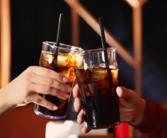 Cheers with two glasses of cola in a cozy restaurant setting