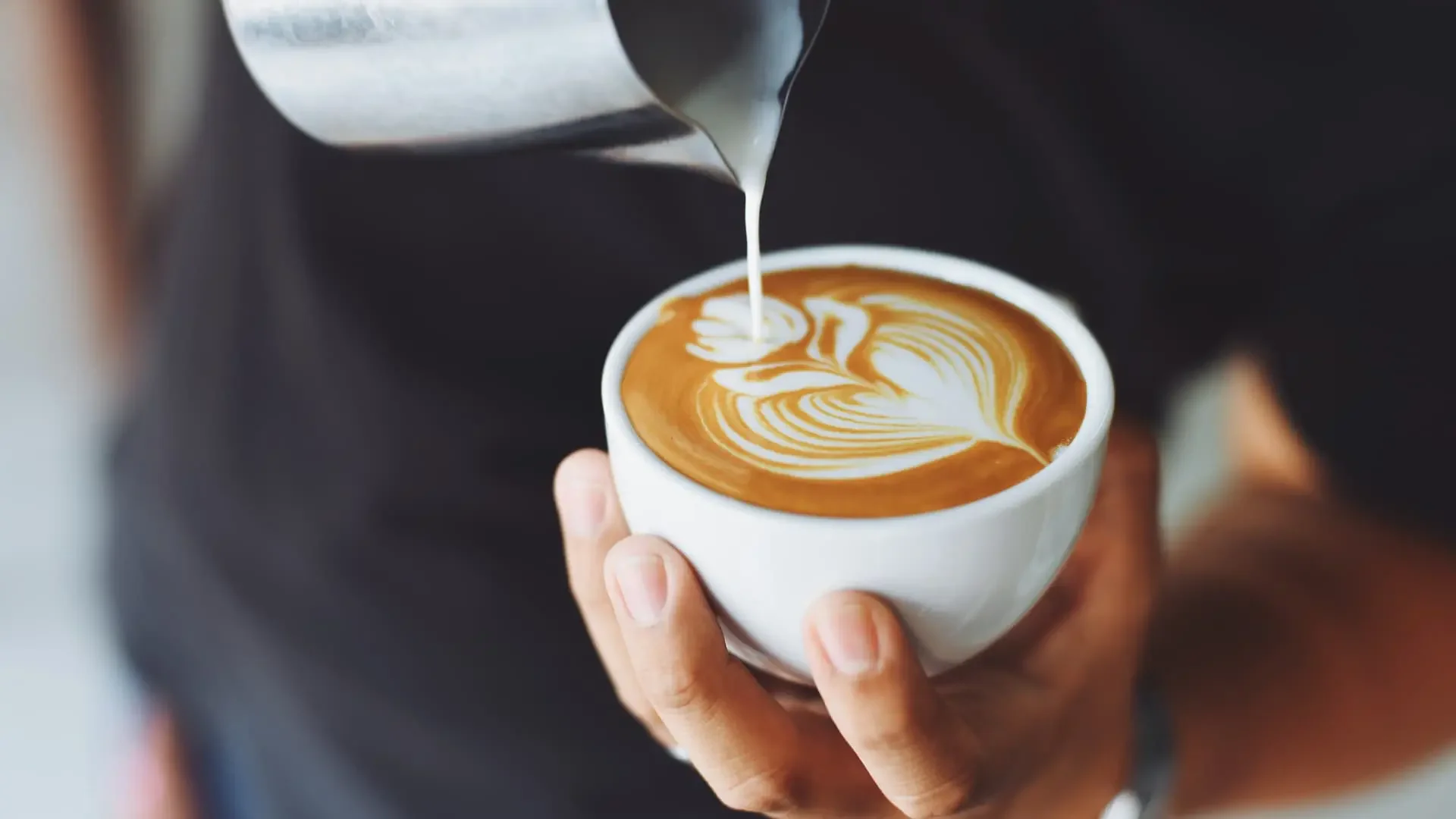 Barista pouring latte art into a white cup