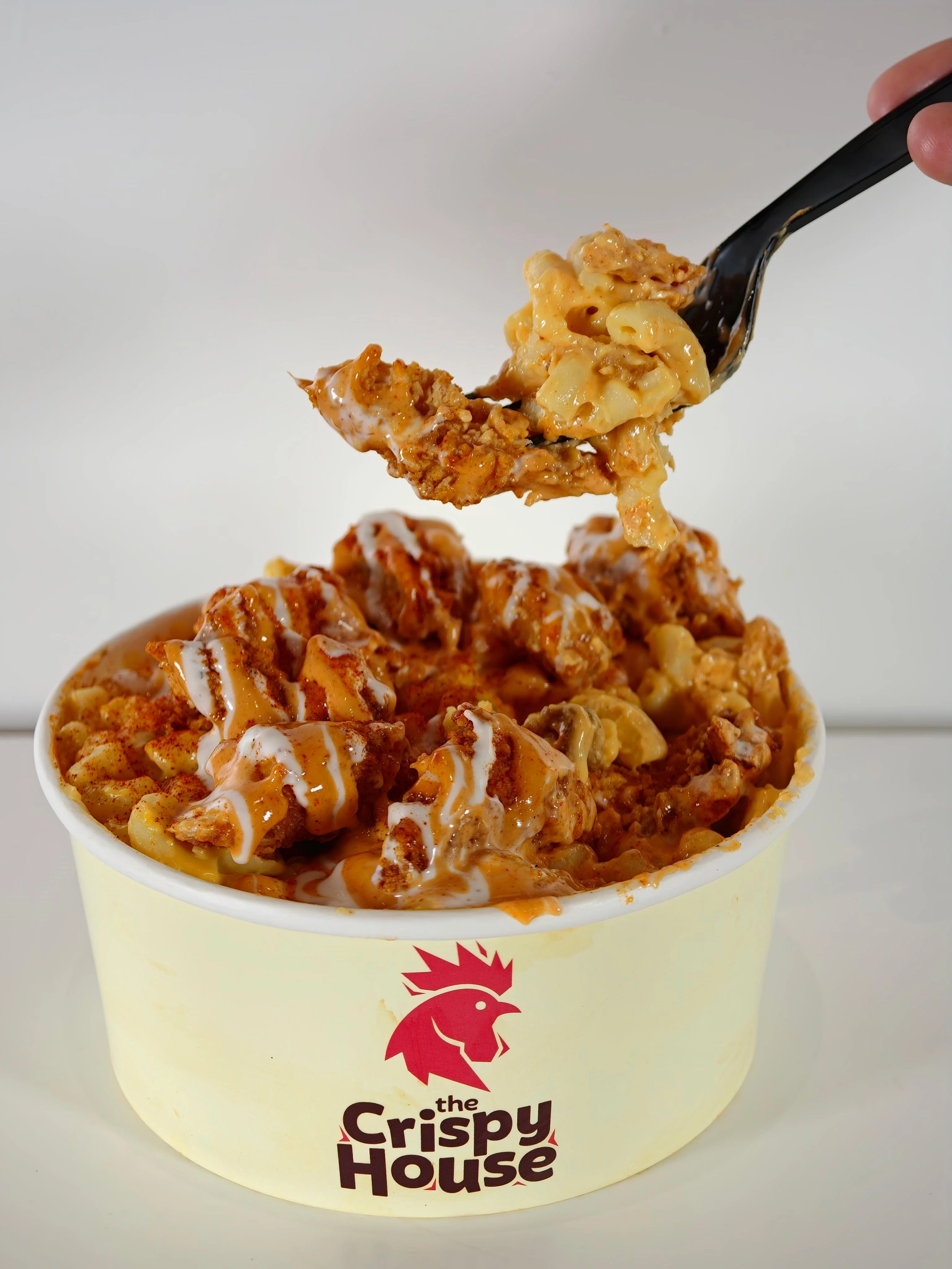 A bowl of macaroni topped with crispy chicken pieces and drizzled with sauce, being served with a fork.