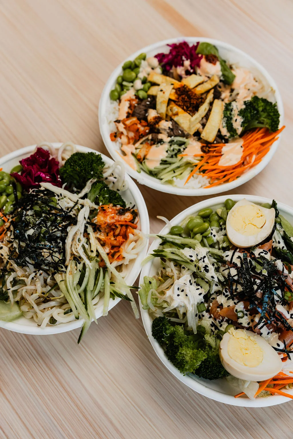 three beautifully built bowls with different meat, toppings and sauces