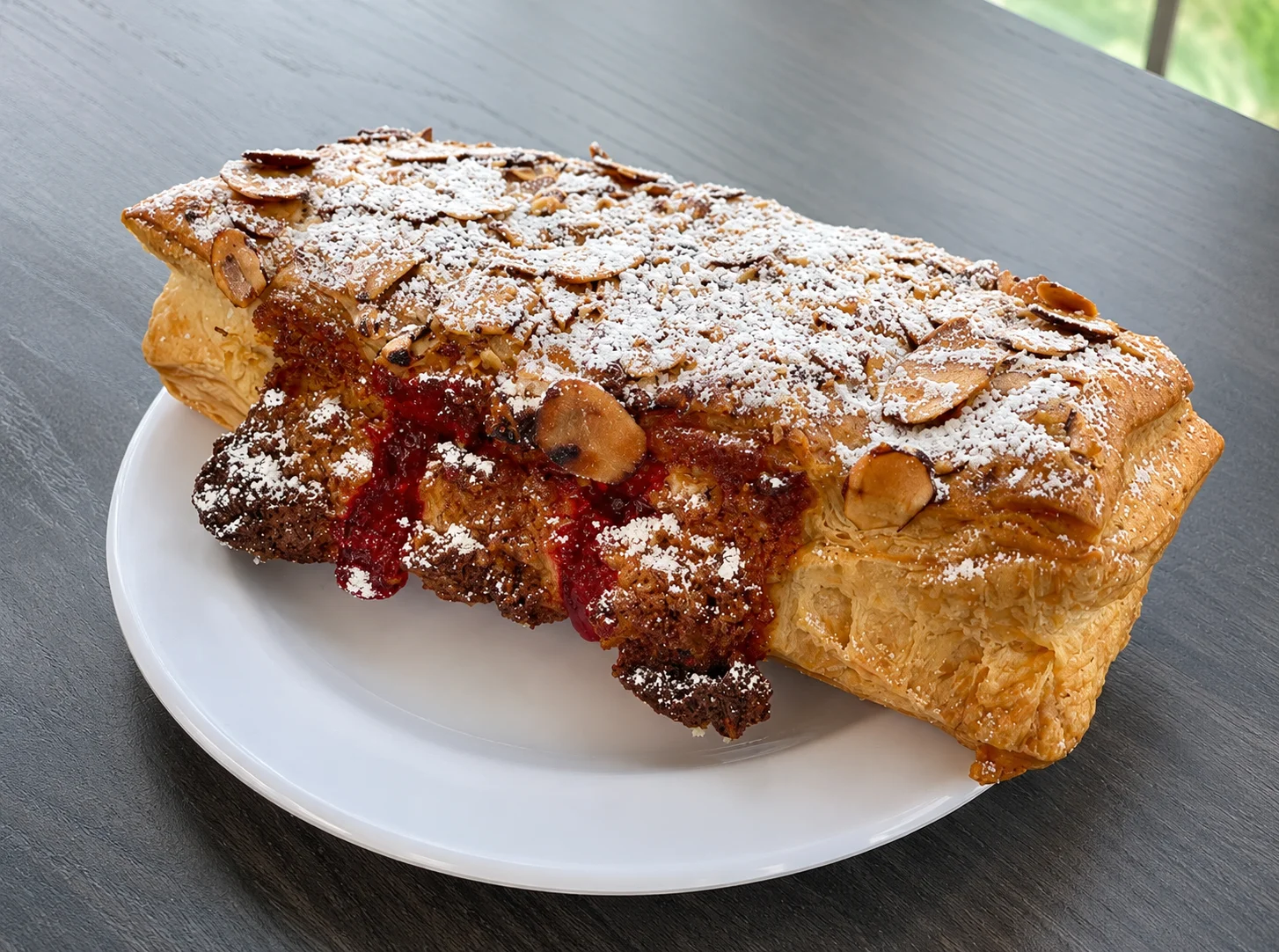 A flaky pastry topped with powdered sugar and sliced almonds.
