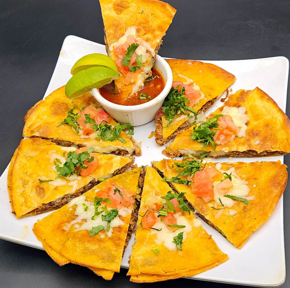 Delicious quesadilla slices with salsa and lime on a white plate.